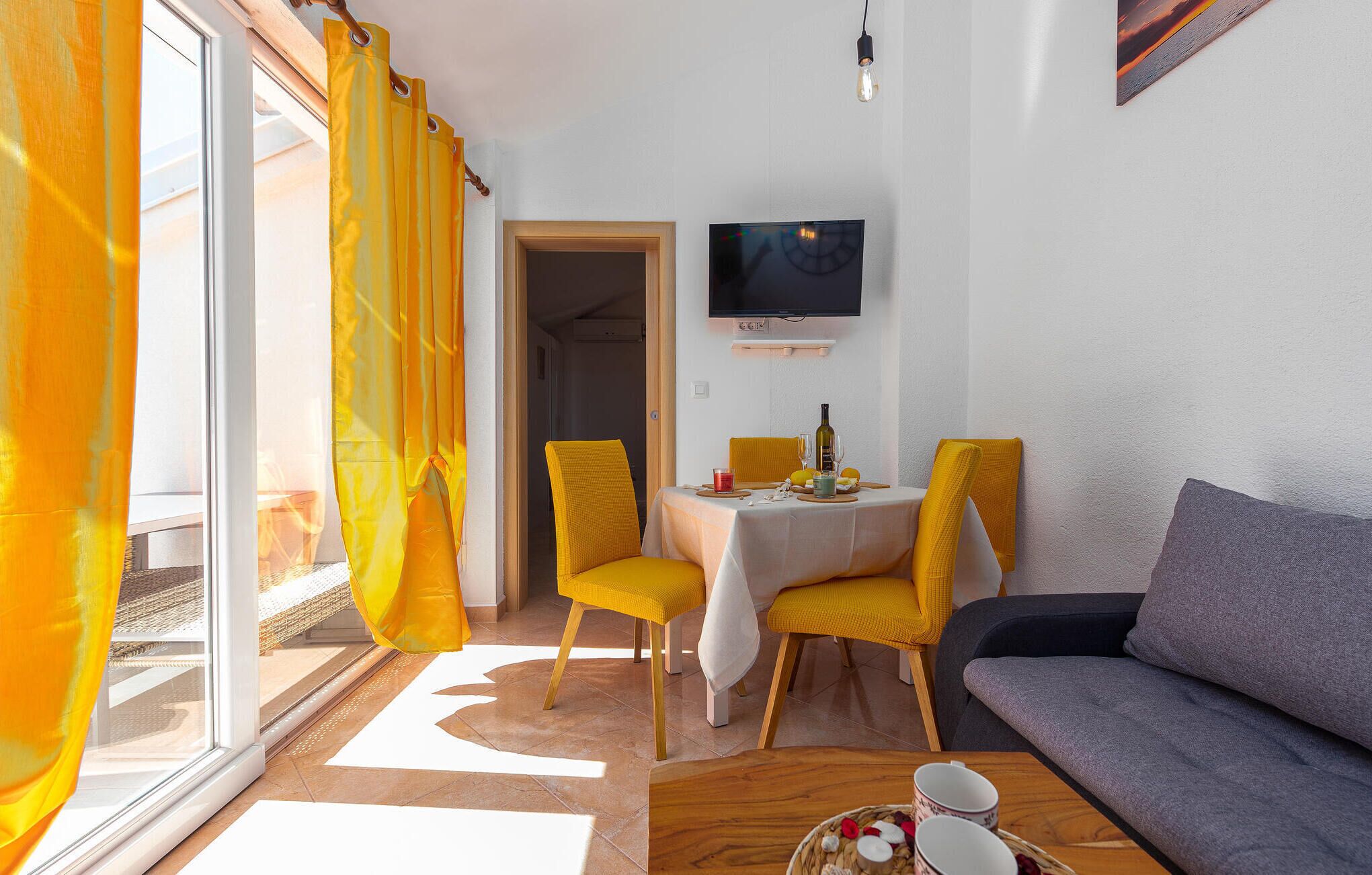 Een kamer met een eettafel, stoelen, een bank, een televisie en een raam met gordijnen.