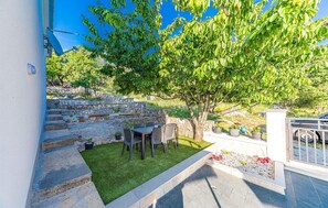 Un patio con un muro de piedra, una mesa y sillas, y un árbol.