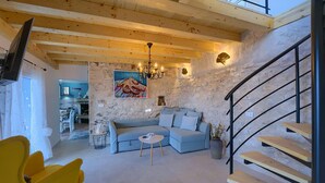 Un salon moderne avec un mur en pierre, un canapé bleu, un fauteuil jaune et un escalier.