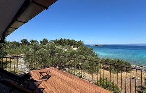 Eine Holzterrasse mit Metallgeländer, die auf eine Küstenlandschaft mit Bäumen und blauem Meer blickt.