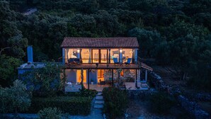 Une maison à deux étages, avec un toit en tuiles, de grandes fenêtres et des fondations en pierre.