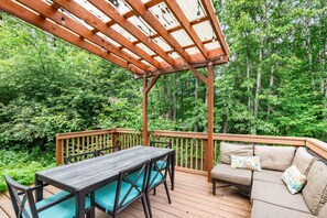 A wooden deck with a table and chairs, surrounded by lush greenery.