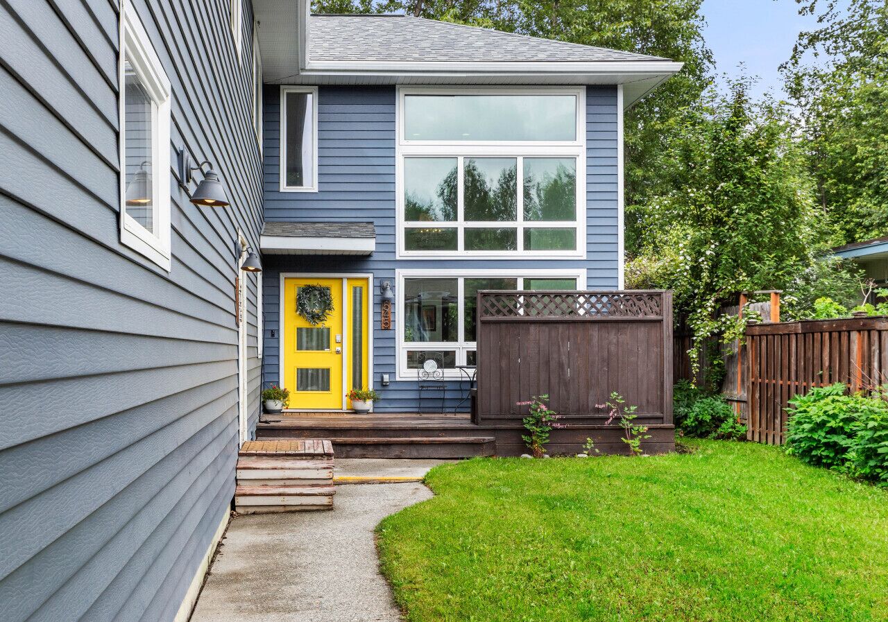 A two-story house with a yellow front door, a wooden deck, and a fenced backyard.