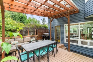 Un patio techado con una mesa y sillas de madera, una parrilla y vista al jardín trasero.