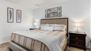 Un dormitorio con una cama grande, una mesita de noche con lámpara y dos plumas enmarcadas en la pared.