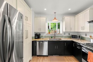 A modern kitchen with stainless steel appliances, black and white cabinetry, and a window providing natural light.