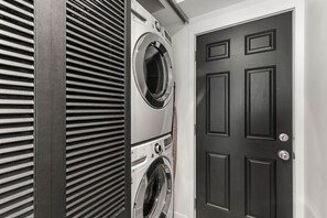A laundry room with two front-loading washing machines and a dark wooden door. - Creekside Retreat, King Bed Near Downtown & Trails, sleeps 14! (Anchorage)