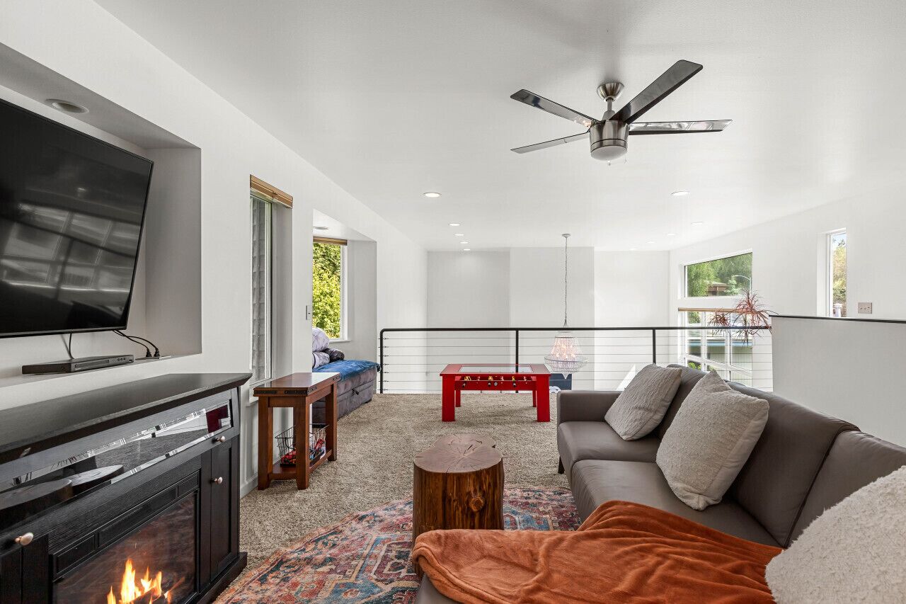 A modern living room with a fireplace, a flat-screen TV, a sofa, a coffee table, and a ceiling fan.