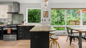 Una cocina moderna con una isla grande, electrodomésticos de acero inoxidable y vistas a un follaje exuberante.