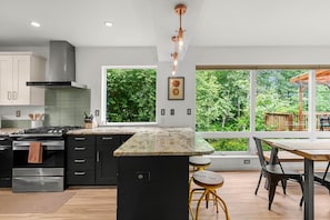 Una cocina moderna con una isla grande, electrodomésticos de acero inoxidable y vistas a un follaje exuberante.