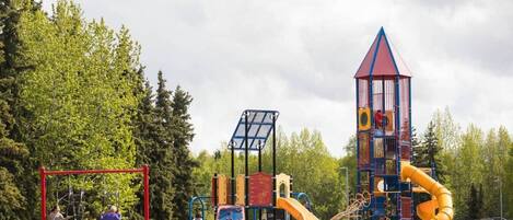 A playground with various play structures including a slide, climbing area, and a tower.