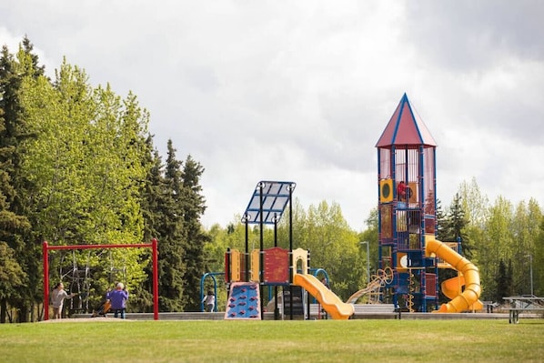 Un parque infantil con diversas estructuras de juego, incluyendo un tobogán, una zona de escalada y una torre.