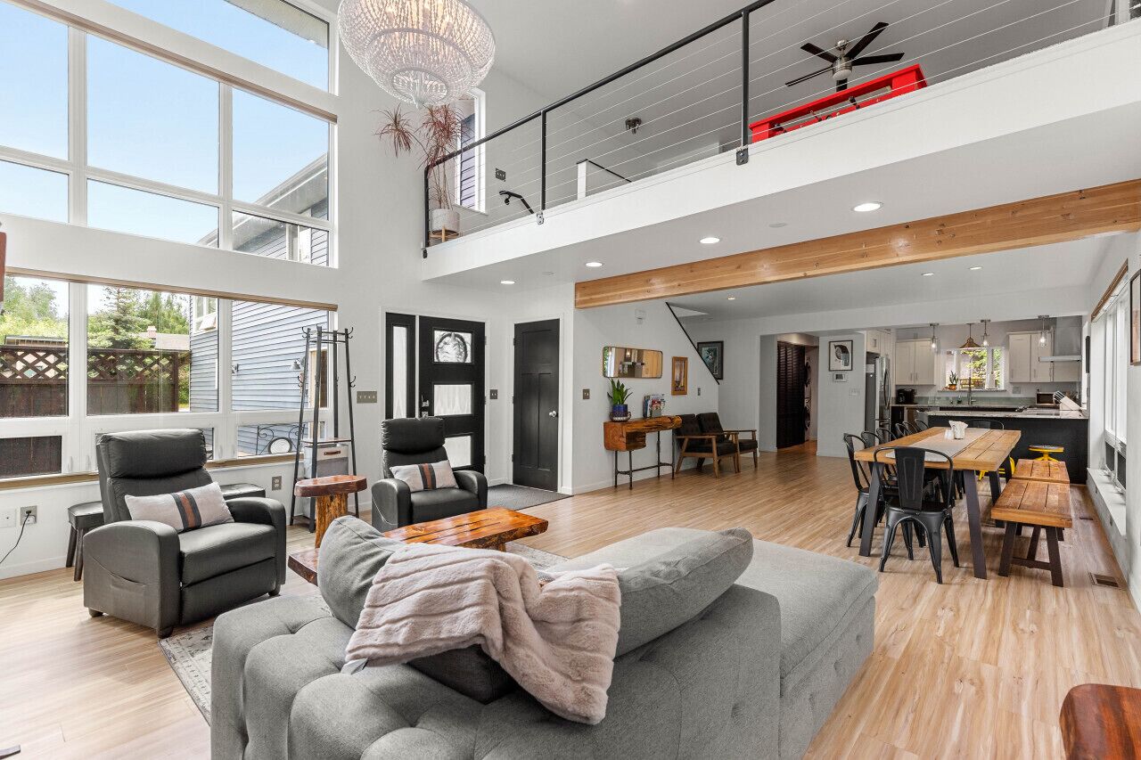 A spacious living area with a high ceiling, a dining table, and a kitchen in the background.