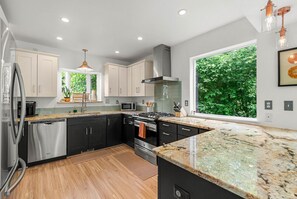 A modern kitchen with stainless steel appliances, black cabinets, and a large window offering a view of greenery.