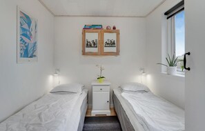 Una habitaci ón pequeña y luminosa con dos camas individuales, un mueble pequeño, un espejo y una ventana con una planta.