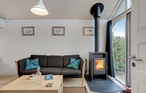 Un salon moderne avec un canapé, une table sur laquelle se trouvent un livre et des lunettes, et un poêle à bois.