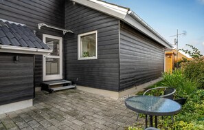 Una casa de exterior oscuro, un patio con baldosas y un pequeño espacio de estar al aire libre.