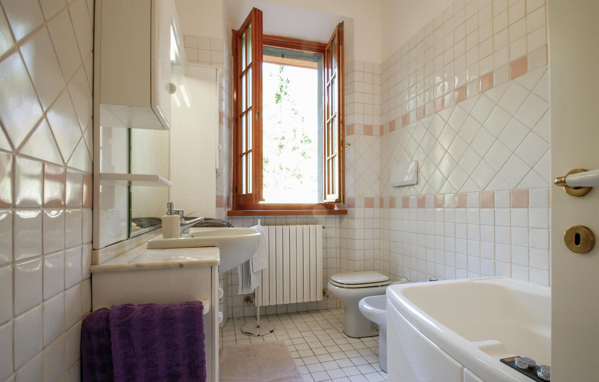 A bathroom with a bathtub, toilet, sink, and a window with an open shutter.