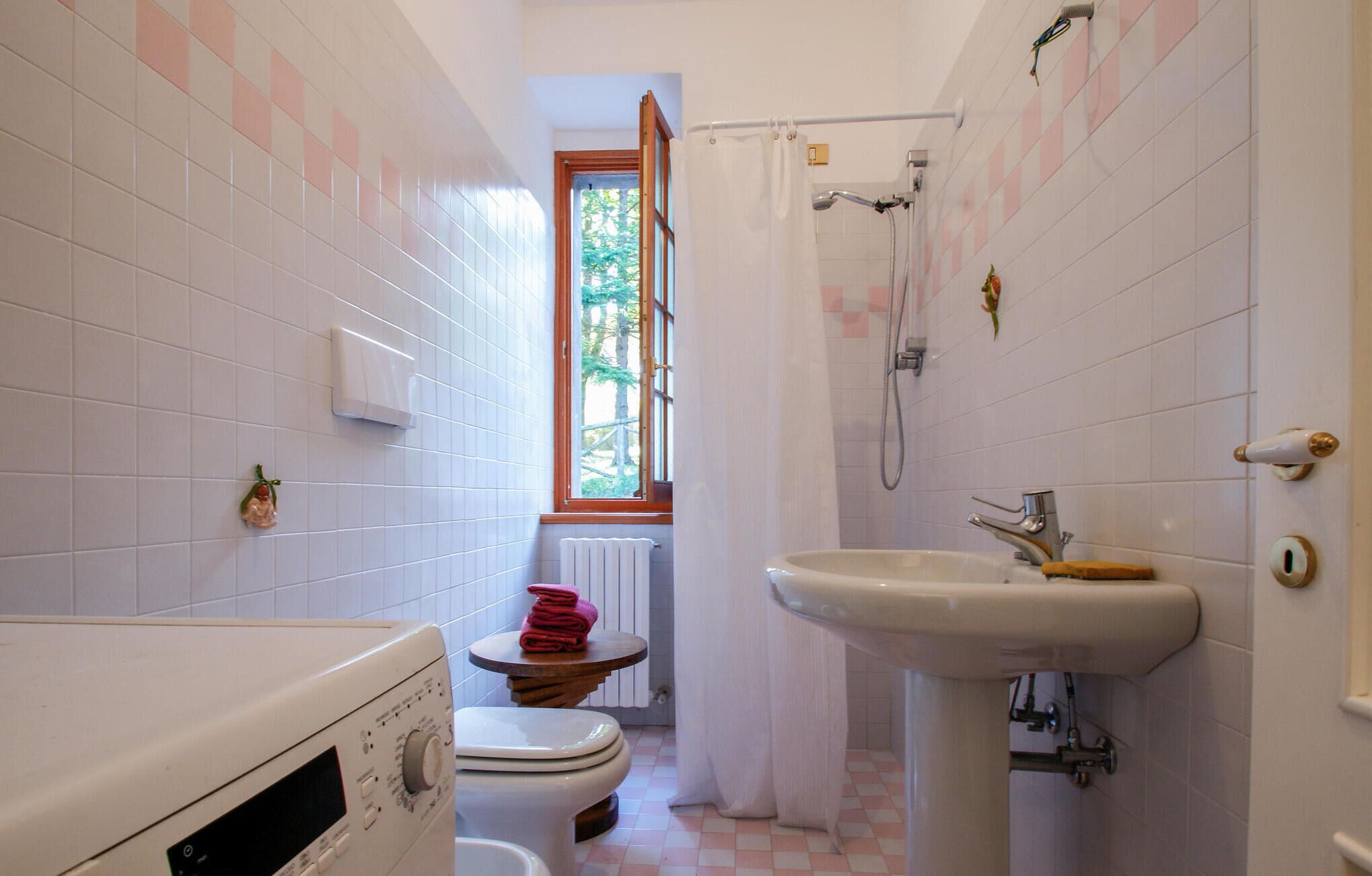 A compact bathroom with a toilet, a washing machine, a sink, and a shower.