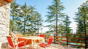Une terrasse avec une table et des chaises, donnant sur une piscine et entourée de grands arbres.