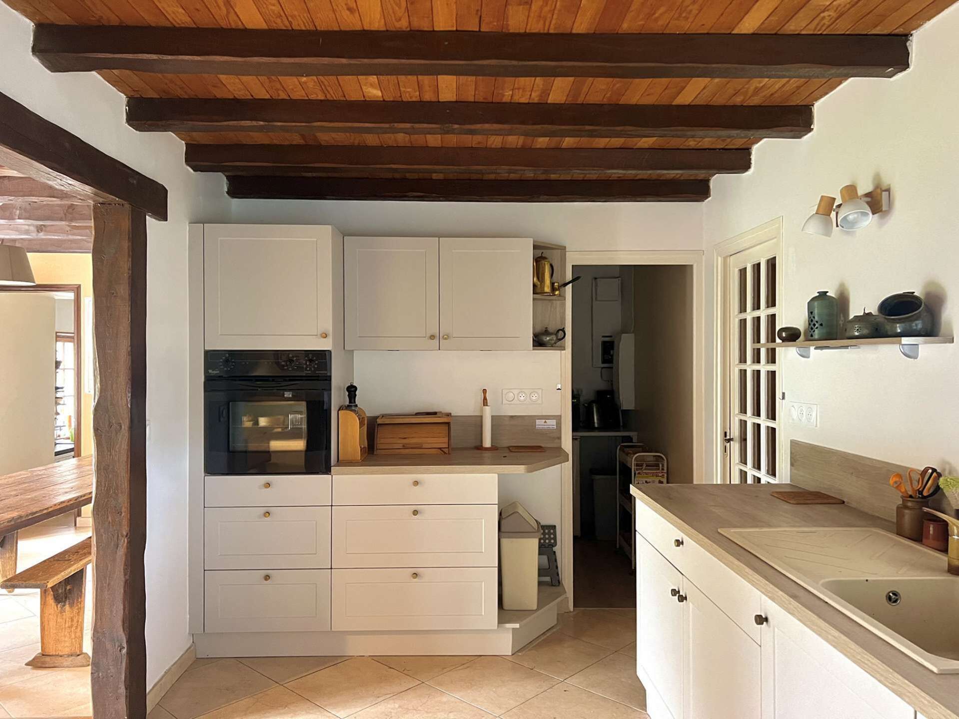 A kitchen with white cabinets, a wooden ceiling, and a tiled floor.