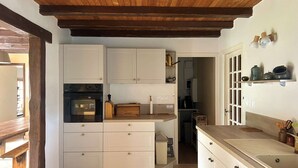 Una cucina con mobili bianchi, soffitto in legno e pavimento piastrellato.