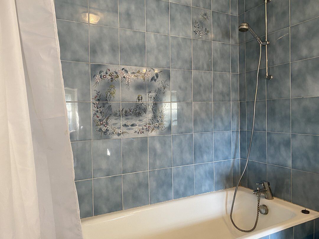 A bathroom with a bathtub, a shower, and a tiled wall with floral patterns.