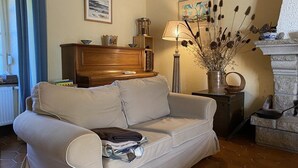Un soggiorno con un divano color beige, un armadio in legno, una lampada e un vaso con fiori secchi.