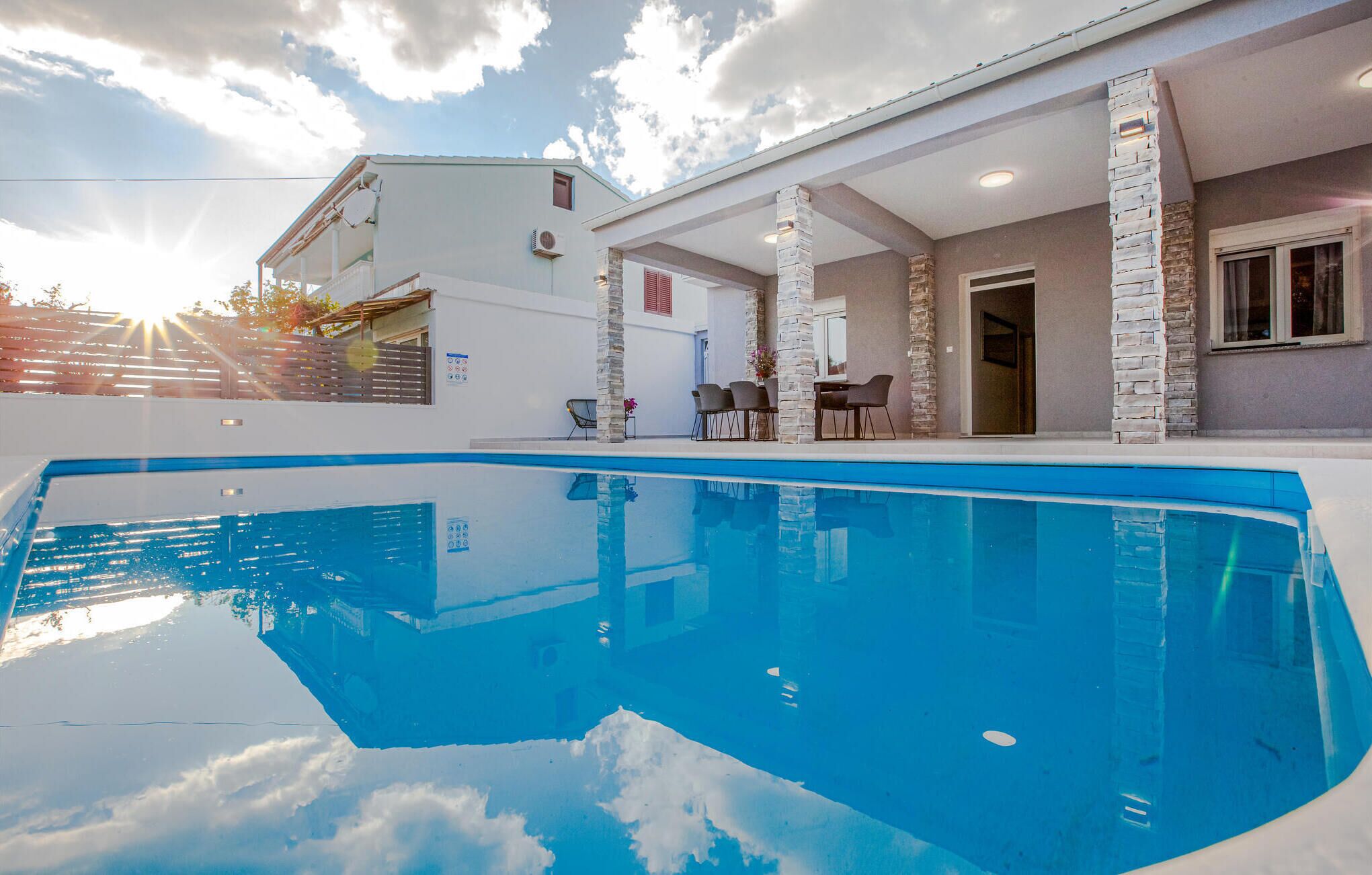 A swimming pool with stone pillars, a covered patio, and a view of the sky.