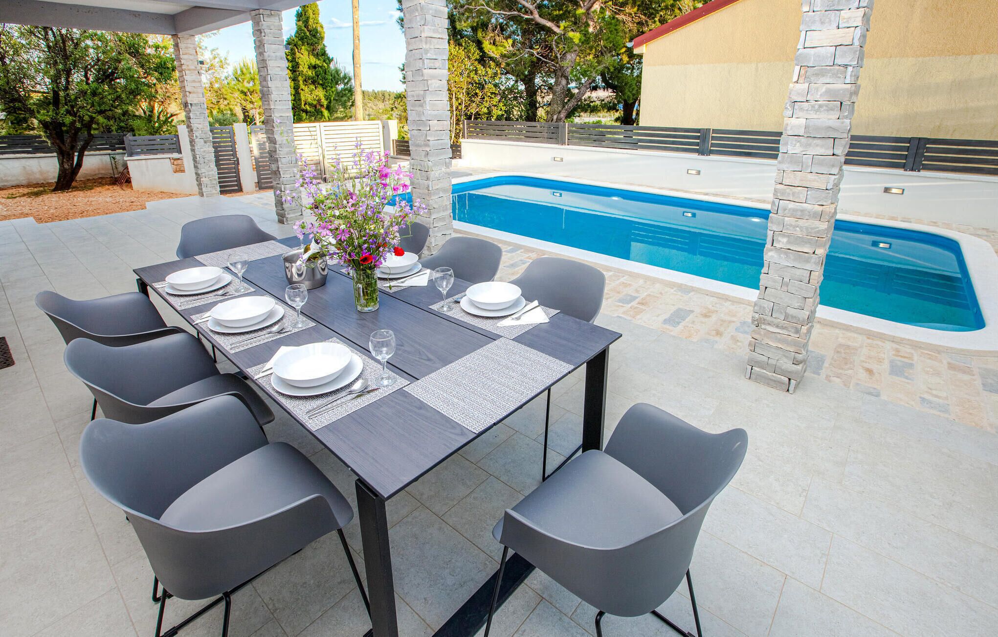 Un espace extérieur aménagé pour les repas, avec une piscine, des piliers en pierre et une table dressée pour six personnes.