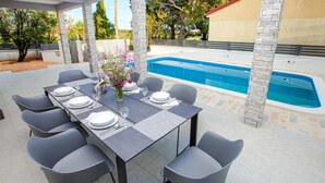 Un espace extérieur aménagé pour les repas, avec une piscine, des piliers en pierre et une table dressée pour six personnes.