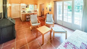 Un vaste espace de vie comprenant une cheminée, une table à manger et un canapé. Au fond, on trouve une cuisine avec une fenêtre donnant sur un jardin.
