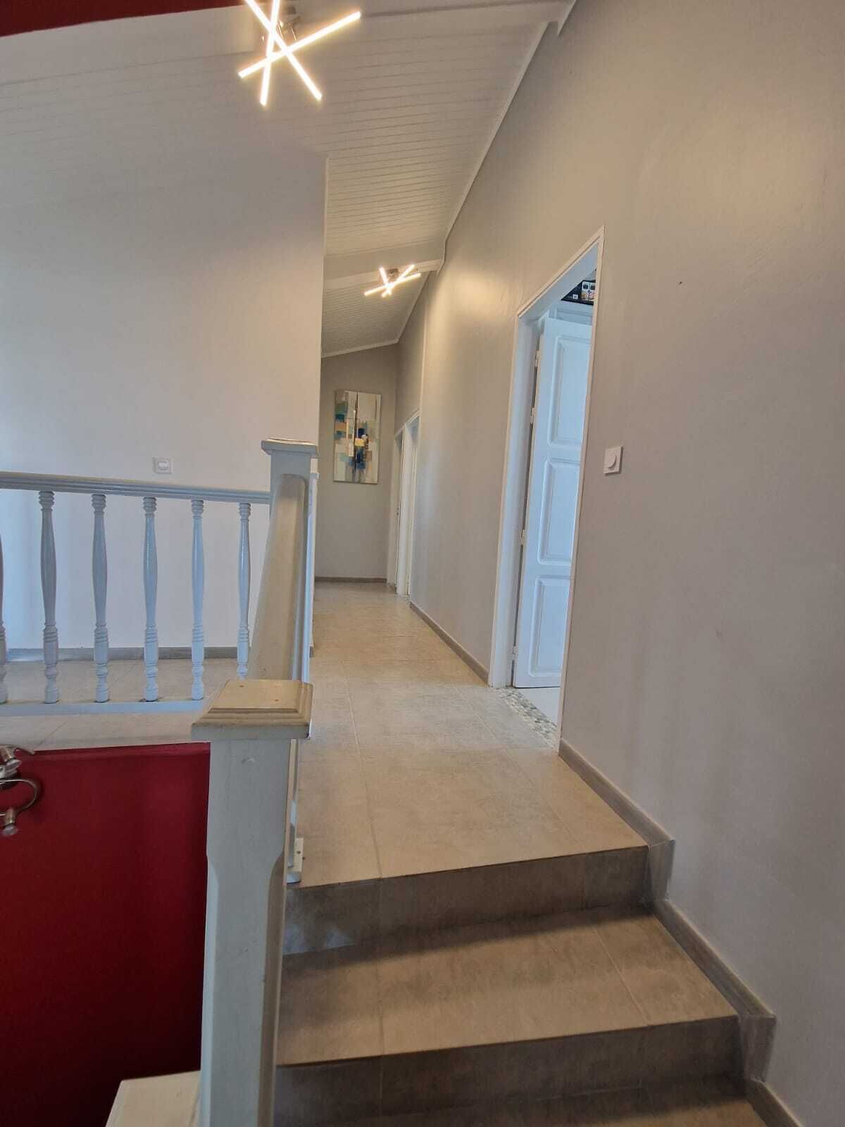En trappa med en röd vägg på ena sidan och en vit vägg på den andra, som leder till en hall med en dörr i slutet.
