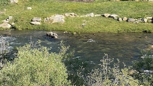 Eine zweistöckige Blockhütte mit Balkon, umgeben von einer Steinschüttung und einem Fluss.