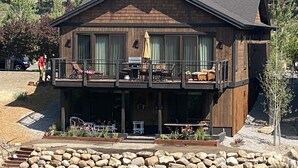 Eine zweistöckige Holzhütte mit Balkon, Sitzgelegenheit im Freien und einer Steinschmalseite.