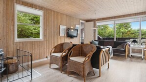 Una habitación con paneles de madera, muebles de mimbre, televisión y ventanas amplias que dan a zonas verdes.