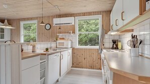 Una cocina moderna con paneles de madera, armarios blancos, un reloj y una ventana con vistas a zonas verdes.