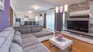 A modern living room with a sectional sofa, a flat-screen TV, and a dining area in the background. - Gorgeous home in Gornje Rastane (Gornje Rastane)