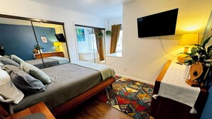 Ett sovrum med en säng, ett skrivbord, en stol, en spegel, en tv, ett fönster med gardiner och en mönstrad matta.