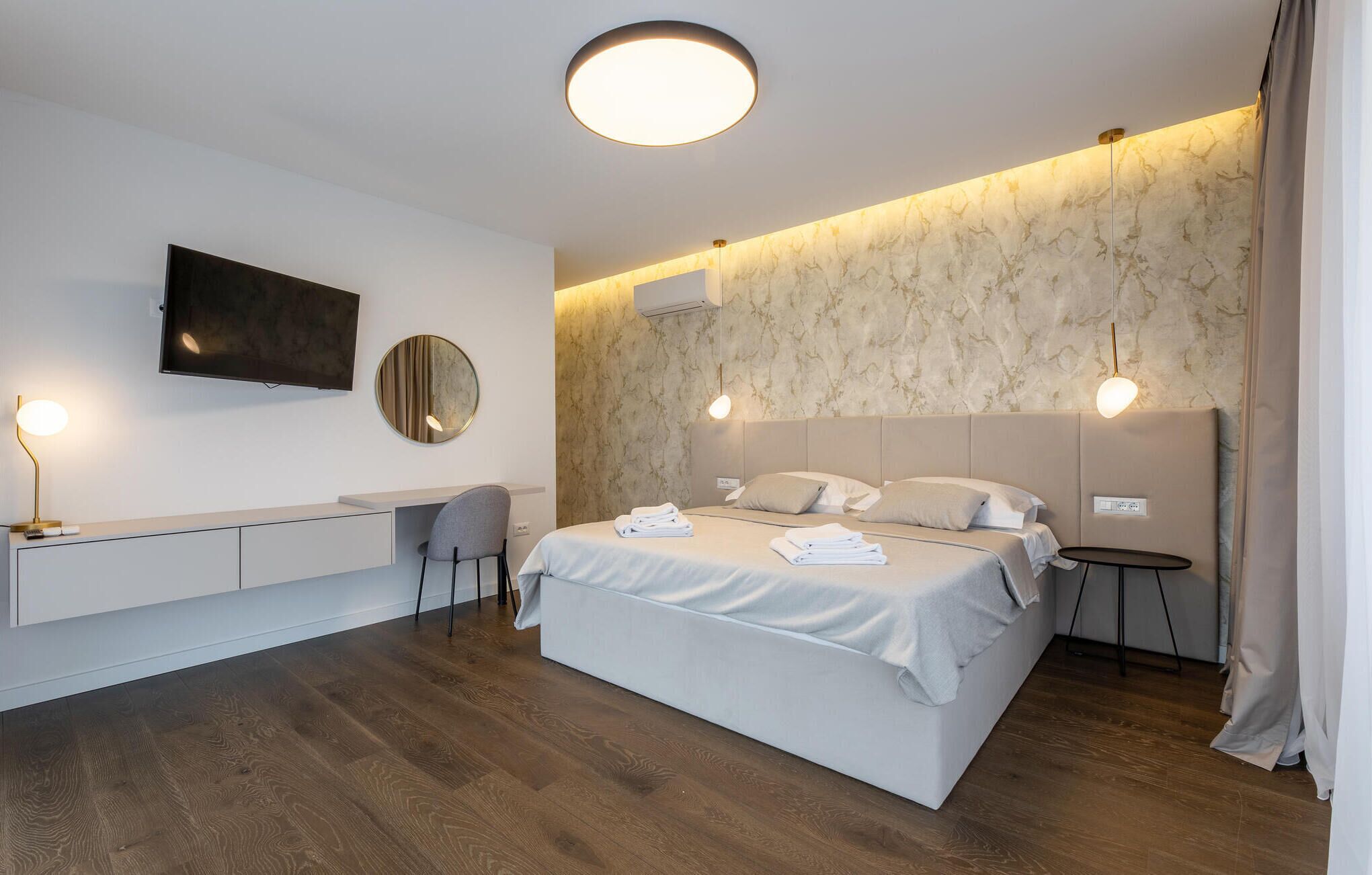 Una habitación de hotel moderna con una cama, mesitas de noche, un escritorio, una silla y un televisor.