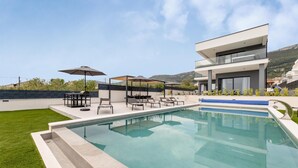 A modern outdoor pool area with a clear view of the pool, lounge chairs, and a barbecue setup. - Nice home in Kastel Stari with sauna (Kastel Stari)