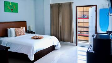 Un cuarto de hotel con una cama, una mesita de noche, una lámpara, un cuadro de pared verde, una ventana con cortinas y vistas al balcón exterior.