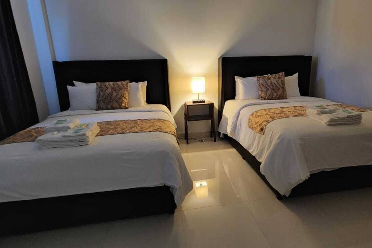 Ein Hotelzimmer mit zwei Betten, jeweils mit Kopfstütze, Nachttisch und Lampe.