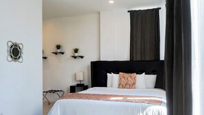 A modern bedroom with a black headboard, white bedding, and a small bedside table with a lamp. - Jovilee Hotel  (Belize City)