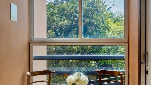 A balcony with a view of trees, a wooden table with chairs, and an air conditioning unit. - Jovilee Hotel  (Belize City)