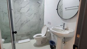 A bathroom with a glass-enclosed shower, a toilet, and a sink with a mirror above it. - Jovilee Hotel  (Belize City)