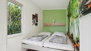 Ein kleines Schlafzimmer mit einem Einzelbett, einem Fenster mit Blick auf Grünflächen, einer grünen Wand und einem Wandteppich.