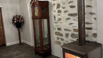 Une pièce avec un mur en pierre, une grande horloge à coucou en bois, un grand meuble en bois et un poêle à bois.