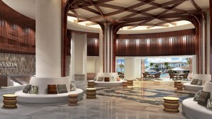 Eine großzügige Lobby mit hohen Decken, markanten Säulen und einer zentralen Sitzecke mit Sofas und runden Tischen.