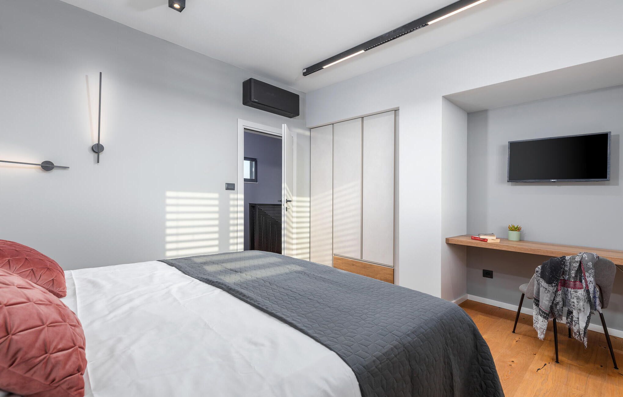 A modern bedroom with a large bed, a desk, a TV, and a wardrobe.
